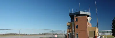 A view of a control tower in a grassy area, with a fence delimiting part of the airport runway.